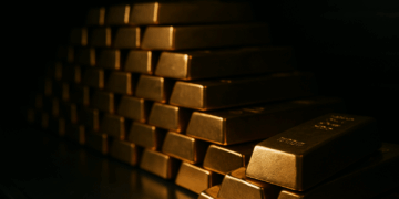 Lingotes de oro apilados en una bóveda oscura con luz suave resaltando el brillo frontal